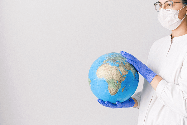 A lady wearing a face mask and medical gloves holds Earth globe.